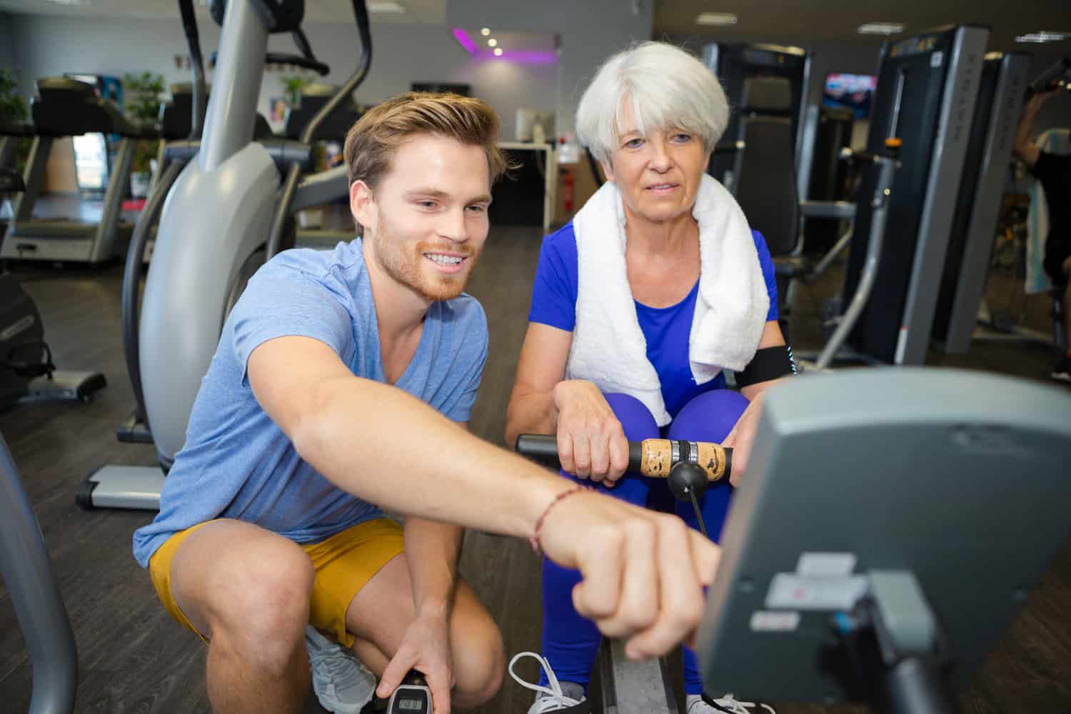 coach and elder lady in the gym using a rowing machine